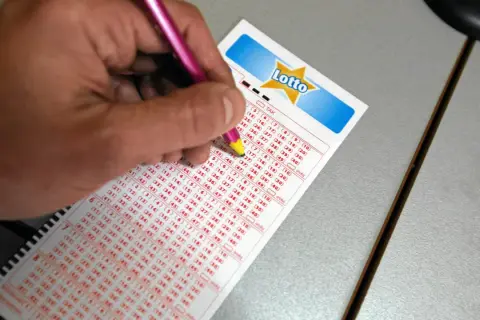 Ręka z ołówkiem zaznacza liczby na kuponie Lotto. Dowiedz się, lotto plus na czym polega dodatkowe losowanie i jak zwiększyć szanse na wygraną.