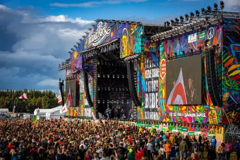 Kolorowa scena festiwalu polandrock 2026 z tłumem fanów. Na ekranach widać artystów, a nad nimi tęczowe grafiki.