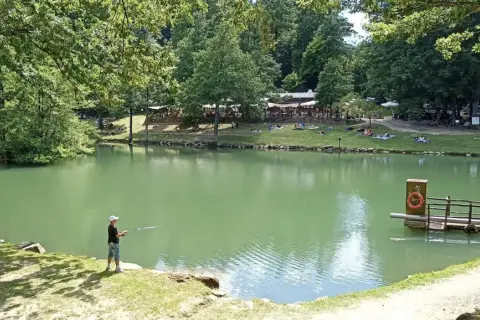 Un ragazzo pesca sul lago Pontini, mentre altre persone si rilassano sull'erba.