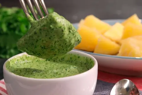 Un tenedor recoge una porción de mojo verde canario, una salsa vibrante, junto a papas arrugadas.