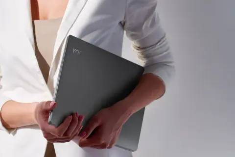Kobieta w białej marynarce trzyma laptopa Lenovo Yoga. Czas na aktualizację systemu, by praca była płynna.