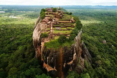 Imponerande ruiner på toppen av en klippa, som en fästning. En vy som påminner om Adams Peak, omgiven av frodig djungel.