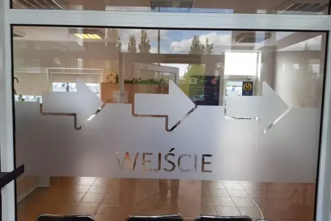 Szklane drzwi z matowymi strzałkami i napisem "WEJŚCIE".