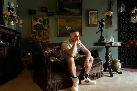 Uomo pensieroso su divano di velluto, circondato da quadri e oggetti d'antiquariato. Forse sta pensando a testi sch cartine Cartier.