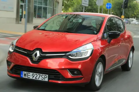 Czerwony Renault Clio 3 1.2 benzyna w ruchu miejskim. Kierowca w okularach przeciwsłonecznych.