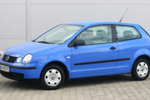 Niebieski Volkswagen Polo 1.2 benzyna, widok z boku. Auto stoi na kostce brukowej przed szarym budynkiem.