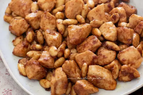 Un invitante pollo alle mandorle, con bocconcini dorati e mandorle tostate, servito su un piatto bianco.