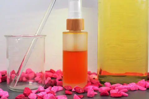 Zutaten für anti aging creme selber machen: ein Becherglas mit Pipette, eine Sprühflasche mit orangefarbener Flüssigkeit und ein großes Glas mit gelbem Öl.