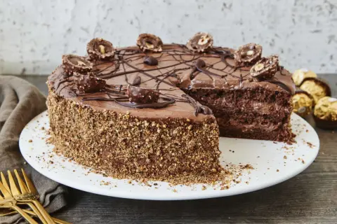 Schokoladentorte mit Ferrero Rocher verziert, die Seiten sind mit gehackten Nüssen bedeckt. Ein Stück fehlt, was Lust auf mehr macht.