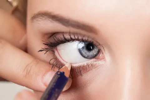 Una mano applica una matita bianca per illuminare la rima interna dell'occhio, un trucco per ingrandire lo sguardo.