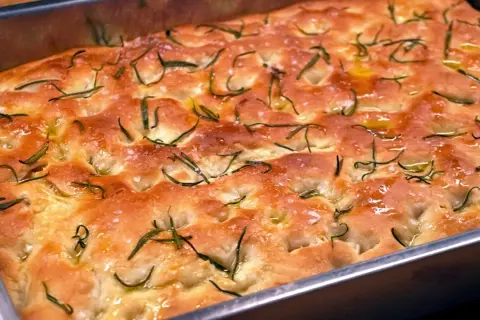 En gyllene focaccia barese med rosmarin och flingsalt i en form. Doftar ljuvligt!