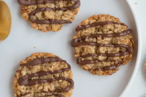 Nyttiga havrekakor utan socker, dekorerade med choklad, ligger på en vit tallrik bredvid guldfärgade skedar.