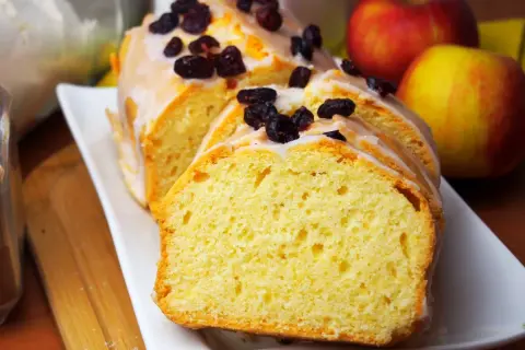 Wilgotna babka na oleju z kakao, polana lukrem i posypana żurawiną, obok jabłek.