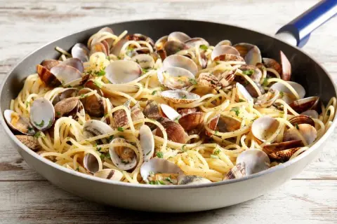 Un piatto invitante di spaghetti con le vongole, condito con prezzemolo fresco, servito in una padella su un tavolo di legno.