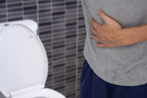 Mężczyzna trzyma się za brzuch, siedząc obok toalety. Może to być objaw raka odbytnicy.