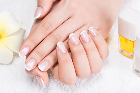 Elegancki manicure french z diamencikami, dłonie zadbane i wypielęgnowane, obok kwiat i lakiery.