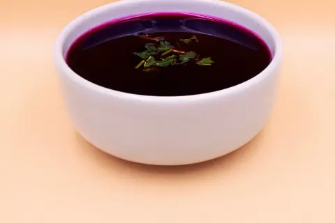 Aromatic barszcz czerwony domowy, głęboki kolor buraków, ozdobiony świeżymi ziołami, w białej miseczce.