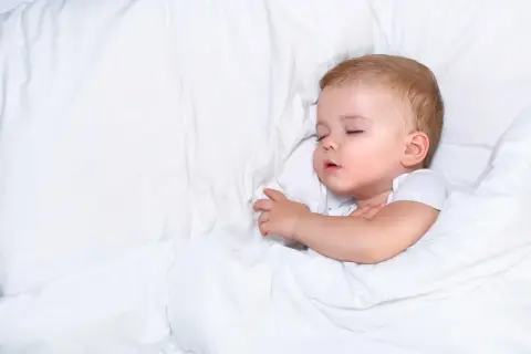 Słodki sen niemowlaka, nawet jeśli czasem towarzyszy mu ciche chrapanie. Maluch odpoczywa otulony białym kocykiem.
