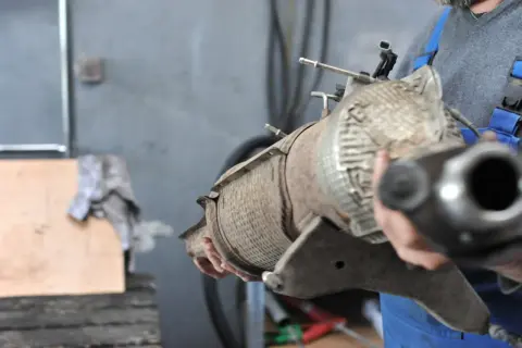Mechanik trzyma zardzewiały element układu wydechowego, prawdopodobnie filtr DPF. Czas na jego wypalanie lub wymianę.