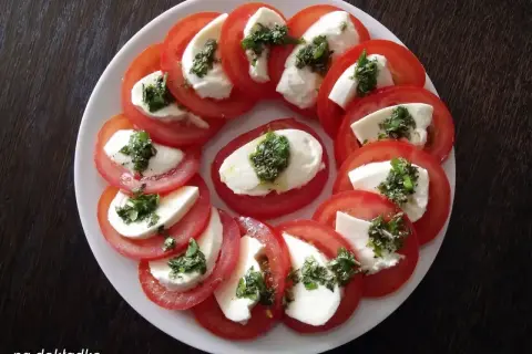 Pyszne pomidory z mozzarellą, ułożone na talerzu, ozdobione ziołami. Idealna przekąska na lato.