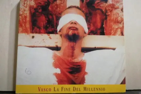 Copertina di "Vasco La Fine Del Millennio" con un uomo bendato e sanguinante, immagine disturbante che evoca la fine di un'era.