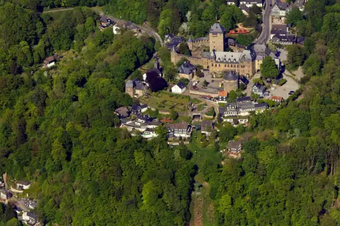 Luftaufnahme eines Schlosses, eingebettet in grüne Wälder. Die Burg ist ein beliebter Ort für Veranstaltungen und Ausflüge.