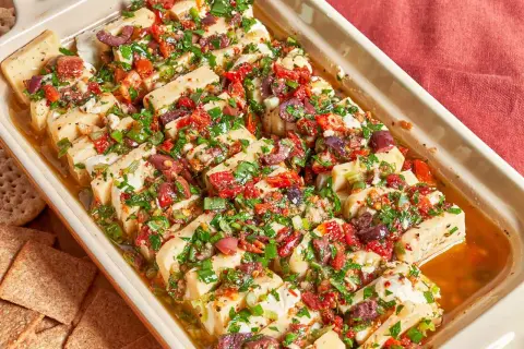 Un plat de fromage blanc coupé en tranches, garni d'olives, de tomates séchées et d'herbes. Une excellente idée repas pour l'apéritif.