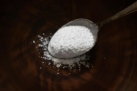 Un cucchiaio pieno di magnesio citrato in polvere bianca, utile per il benessere.