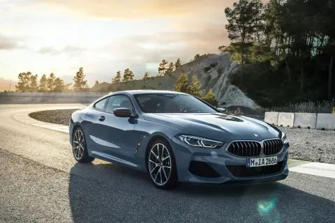 Szary BMW 840d na zakręcie toru wyścigowego, z drzewami i skalistym zboczem w tle.