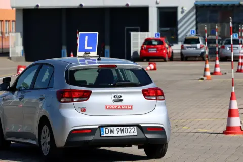 Srebrny samochód z literą "L" na dachu, gotowy do egzaminu. Dofinansowanie do prawa jazdy może pomóc w nauce jazdy na takim pojeździe.