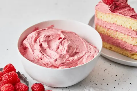 Schüssel mit cremiger Buttercreme mit Pudding und Himbeeren. Daneben ein Stück Kuchen mit derselben Füllung.