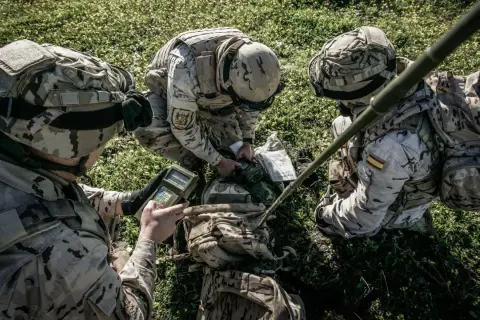 Soldados del ejército español con uniforme multicam revisan equipo en el campo.