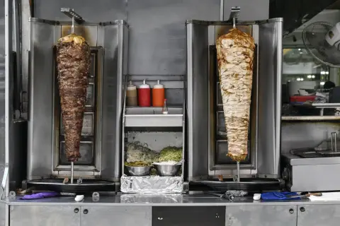 Dwa pionowe rożna z mięsem do kebaba, jeden z wołowiny, drugi z kurczaka. Obok sosy i surówki. Zastanawiasz się, ile kosztuje mały kebab?