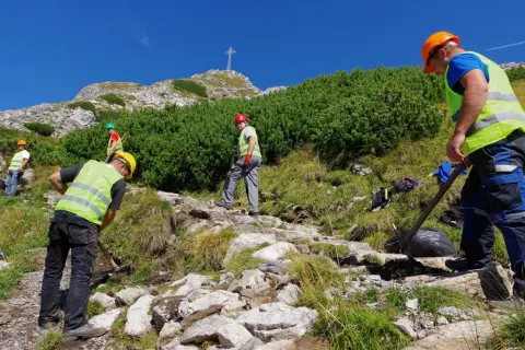 Pracownicy konserwują szlak na Giewont. Czy szlak na Giewont jest trudny? Widać krzyż na szczycie, a teren jest kamienisty.