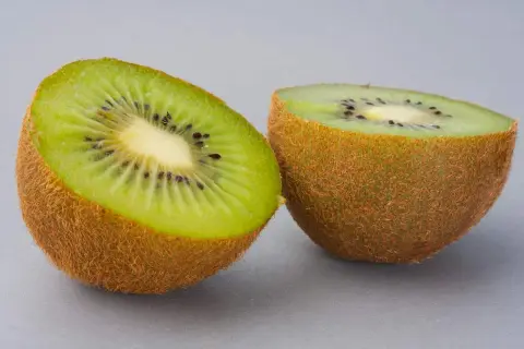 Dwa połówki kiwi na szarym tle. Zastanawiasz się, ile kalorii ma kiwi? To niskokaloryczny owoc, idealny na zdrową przekąskę.