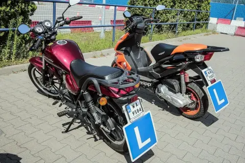 Dwa pojazdy z literą "L" na tablicy, gotowe do nauki jazdy. Czerwony motorower i pomarańczowy skuter.
