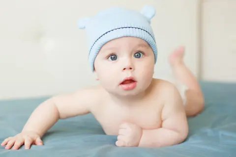 Adorable bébé garçon, prénom S, porte un bonnet bleu avec des oreilles. Il est couché sur le ventre, les yeux grands ouverts.