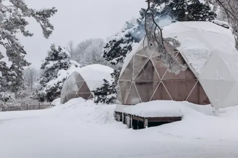 Śnieżne krajobrazy i przytulne domki do wynajęcia na weekend. Dym unosi się z komina jednego z igloo, zapraszając do środka.