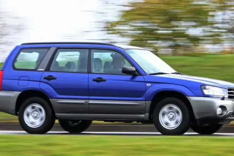 Niebieskie auto 4x4 Subaru Forester z napędem na cztery koła pędzi po drodze, otoczone zielenią.