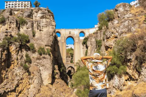 Un hombre con sombrero blanco admira el Puente Nuevo de Ronda en un día soleado.