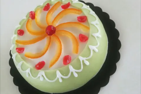 Gâteau sicilien vert pâle glacé, décoré de zestes d'orange, de fruits confits rouges et de glaçage blanc.
