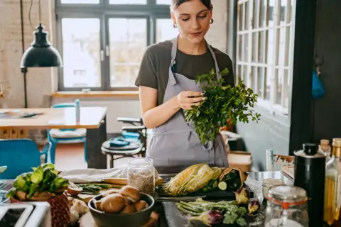 Frau bereitet frisches Gemüse für eine gesunde Ernährung zu. Kräuter, Mais und Pilze auf dem Tisch, inspiriert von der planetary health diet.