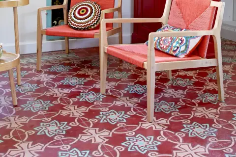 Sol rouge orné de motifs géométriques complexes, typiques des pose carreaux de ciment. Deux fauteuils orange vif avec coussins colorés.