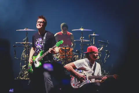 Blink 182 heute: Mark Hoppus spielt Bass, Travis Barker am Schlagzeug, Tom DeLonge mit Gitarre. Energiegeladener Auftritt!