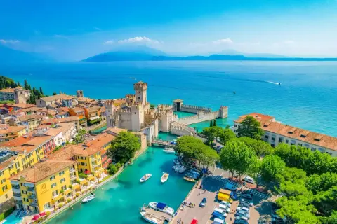 Garda città: castello Scaligero sull'acqua turchese, case colorate e barche ormeggiate.