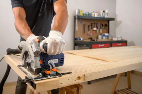 Hombre con guantes usa sierra circular para cortar una puerta de madera. Aprende como enderezar una puerta de madera con esta técnica.