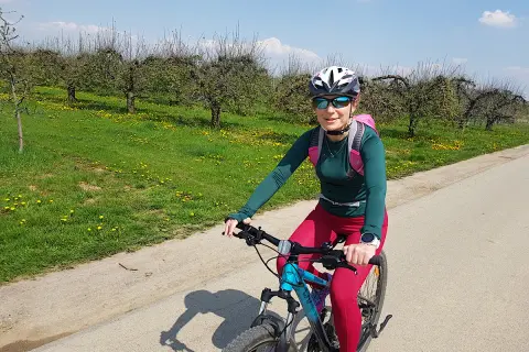 Kobieta na rowerze podziwia sandomierskie trasy rowerowe wśród kwitnących sadów.