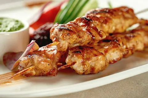 Brochettes de poulet grillées, juteuses et dorées, servies avec une sauce verte et des légumes croquants. Un délice à savourer !