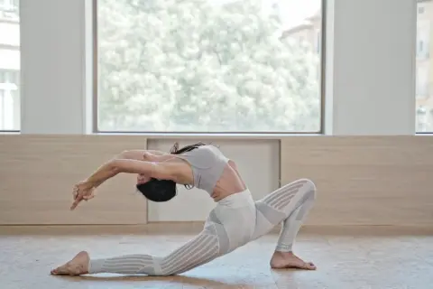 Mujer en postura de Anjaneyasana yoga, arqueando la espalda y extendiendo brazos hacia atrás.