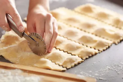 Hände schneiden mit einem Teigrädchen frische Ravioli. So einfach ist ravioli selber machen.